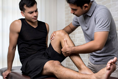 Therapist treating injured knee of handsome athlete male patient